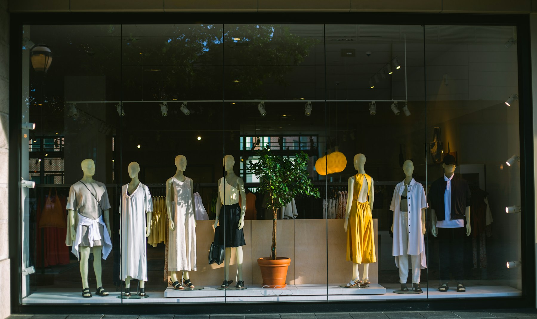 Mannequins dressed in neutral clothing behind a large boutique shop window