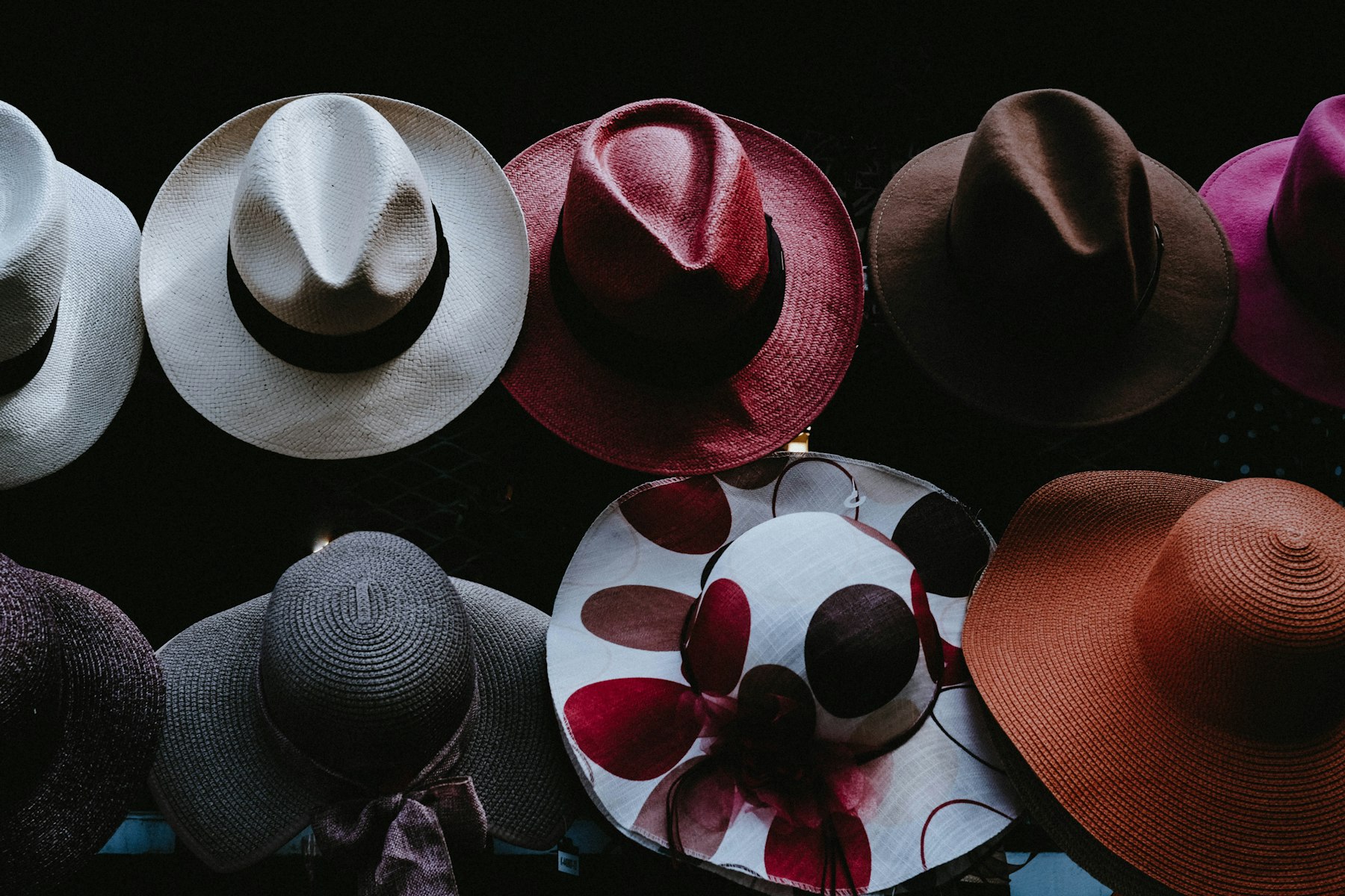 An overhead arrangement of wide-brimmed felt and straw hats against a dark background