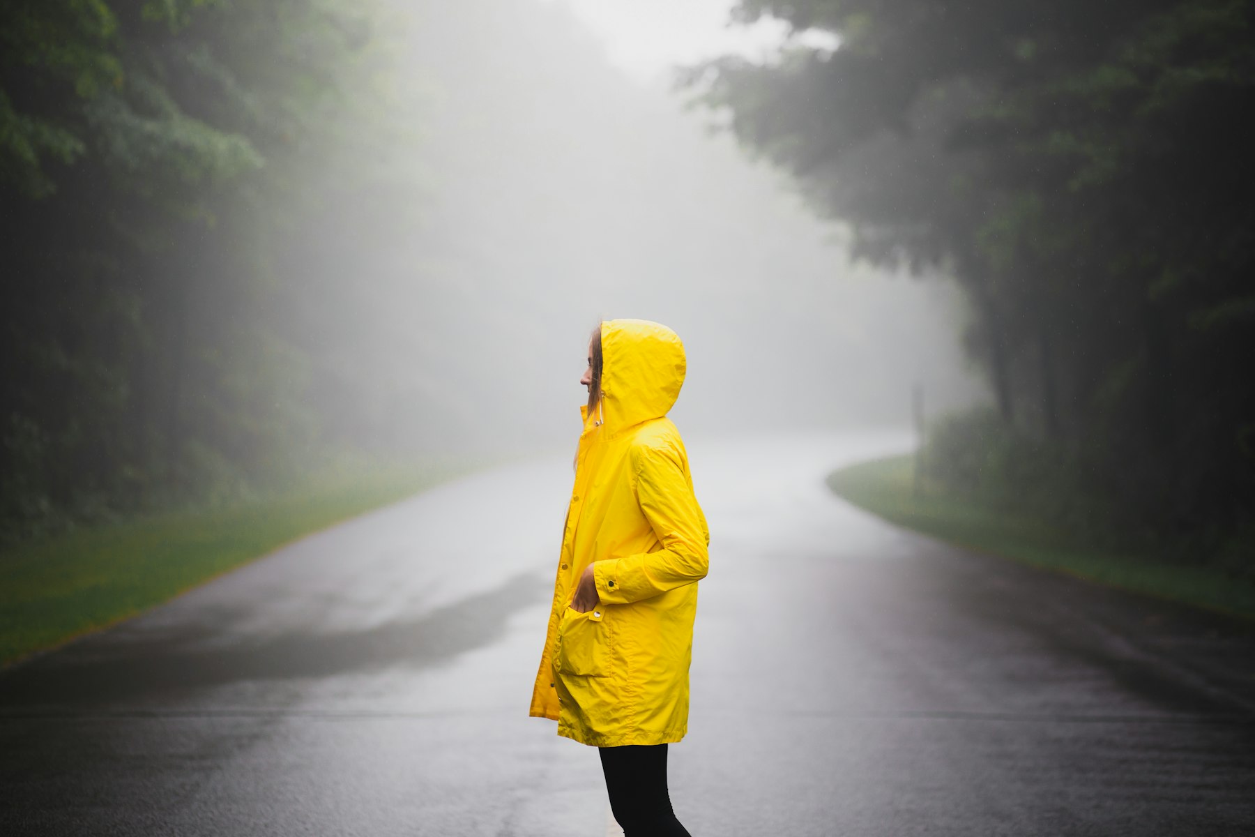 A person in a yellow hooded raincoat on a wet road surrounded by mist and rain