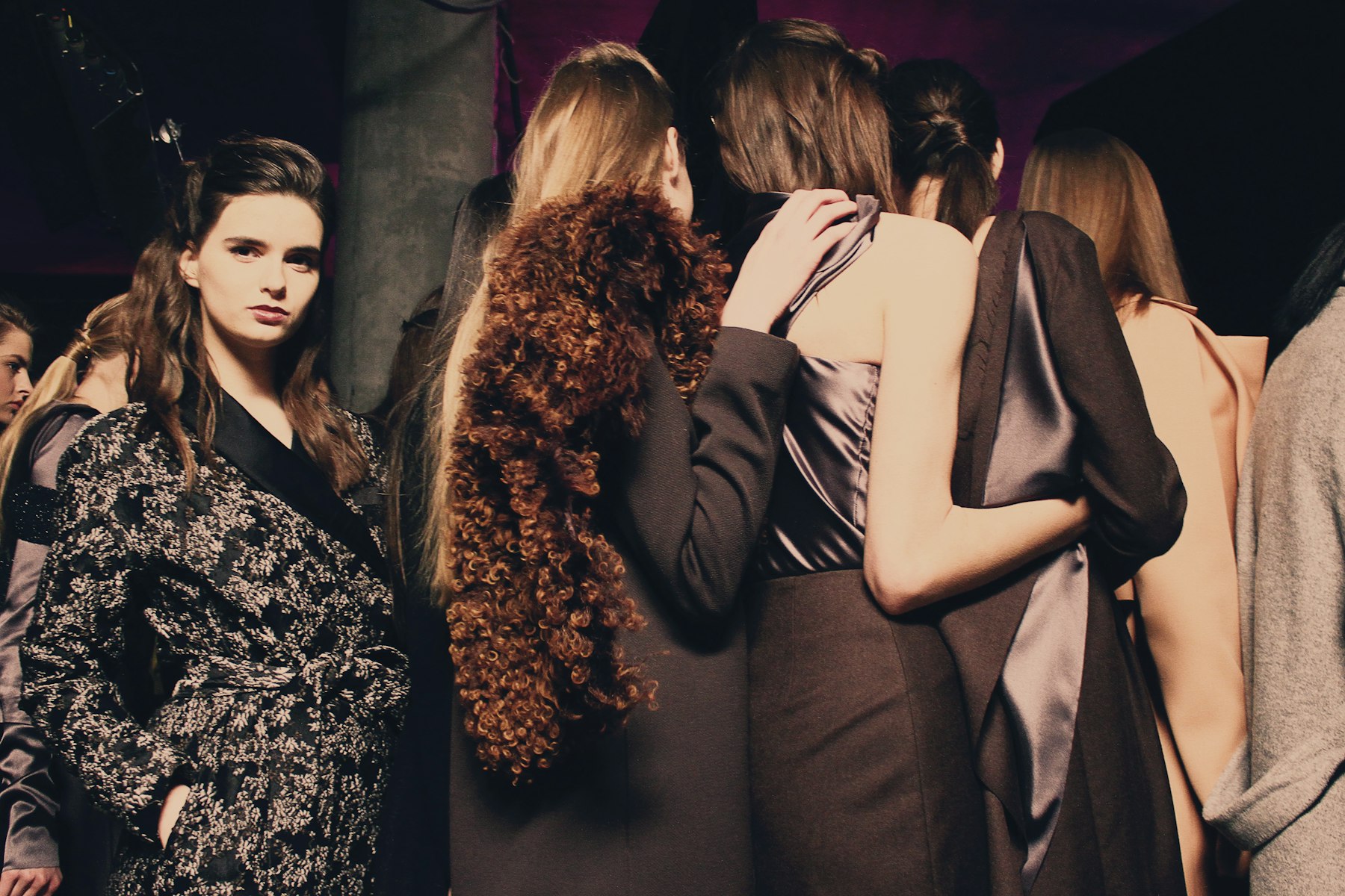 Models waiting backstage at a fashion show in dark wool tailoring, shearling and satin