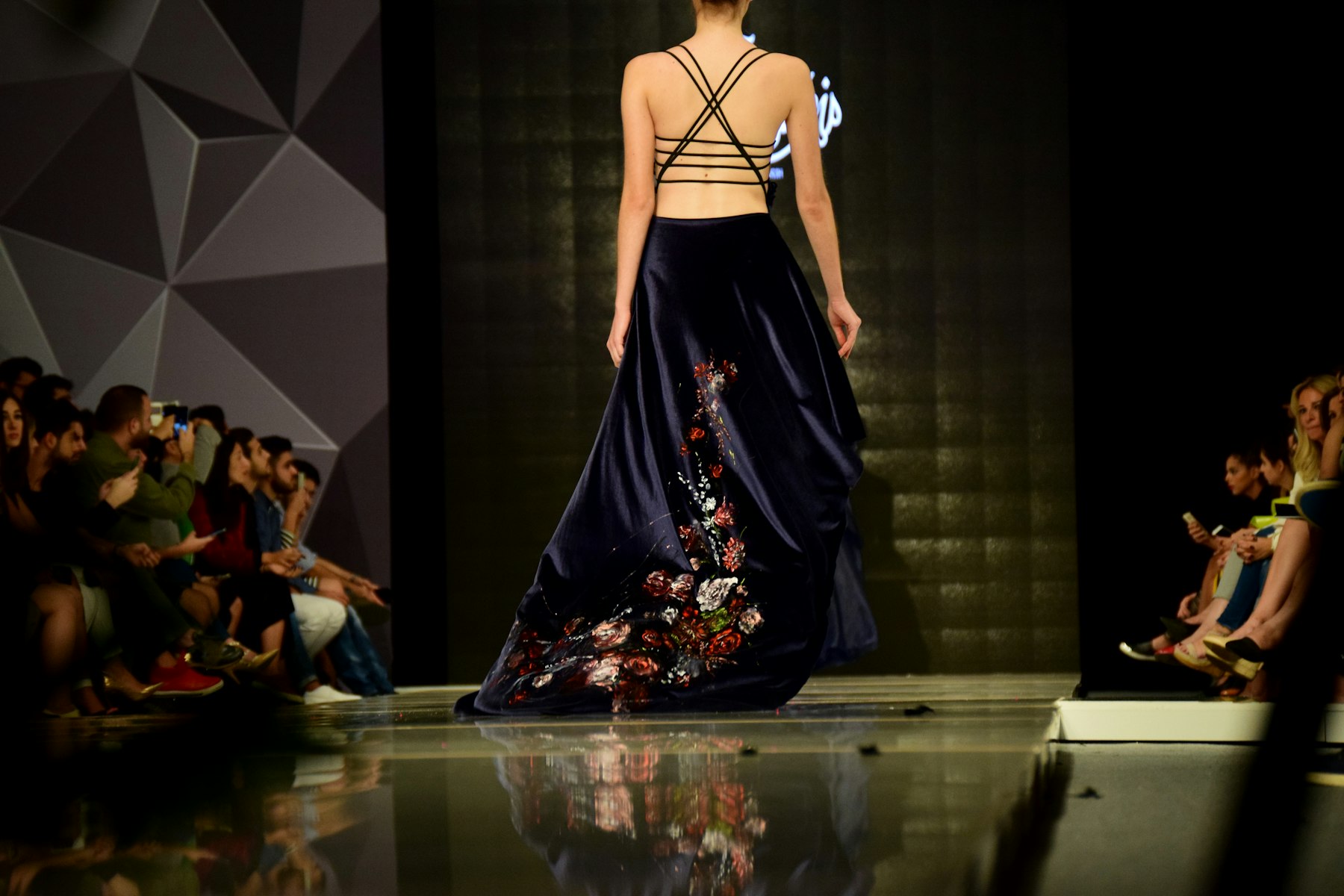A model walking a darkened runway in a navy velvet gown embroidered with red and white flowers