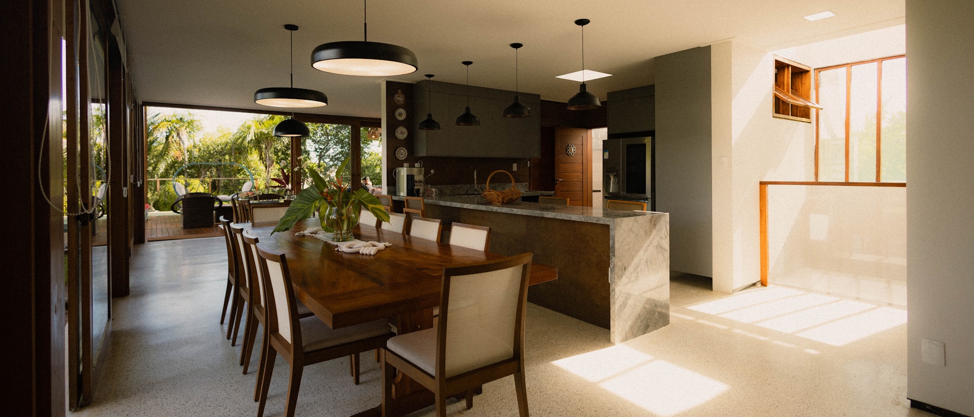 An open-plan kitchen and dining space with a long wooden table, a marble-clad island and glazed doors opening to a garden