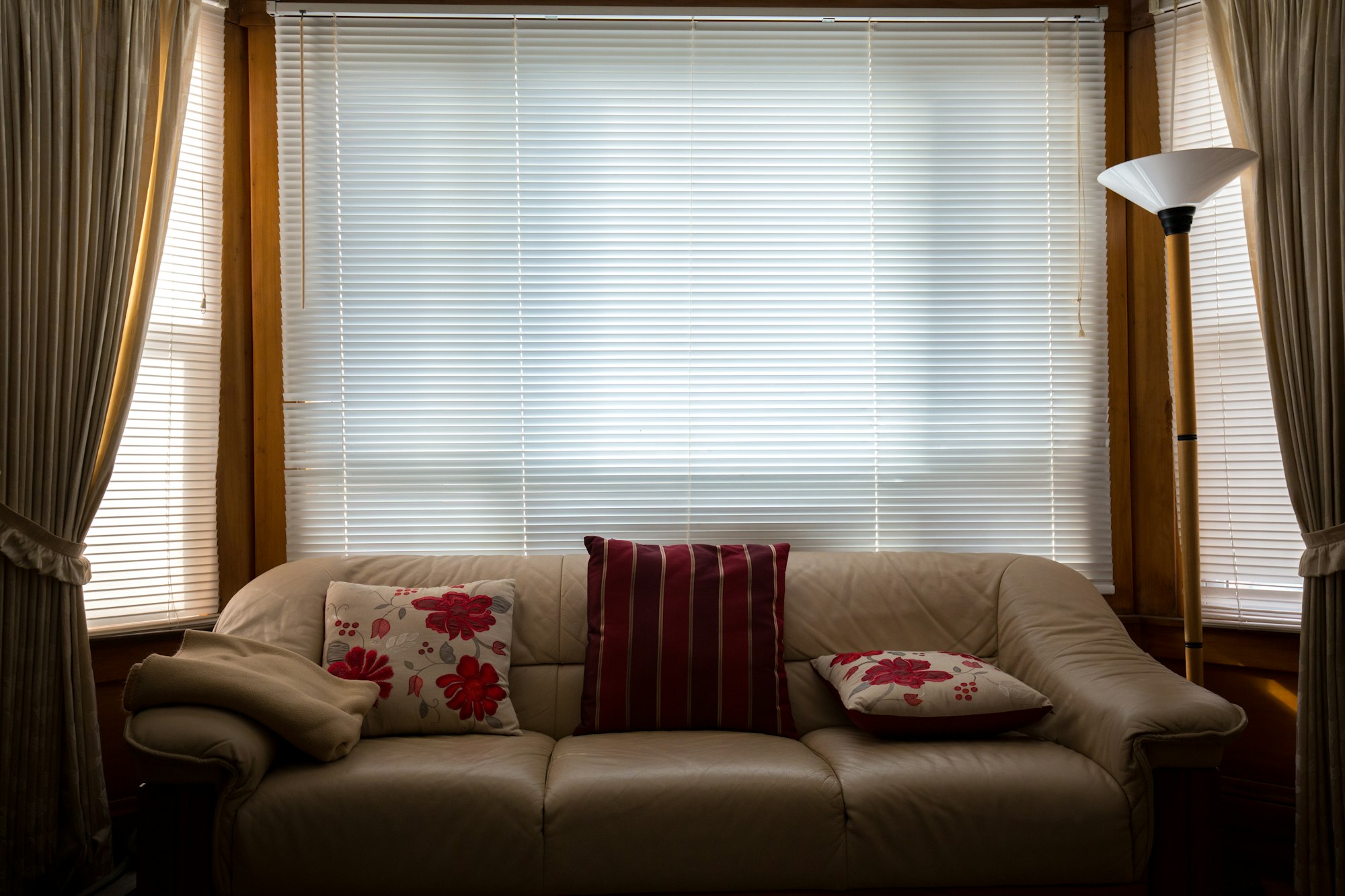 A leather sofa in front of a wide window where bright sunlight floods through closed venetian blinds