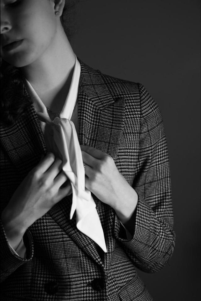 Hands knotting a soft white tie over a checked jacket, in black and white