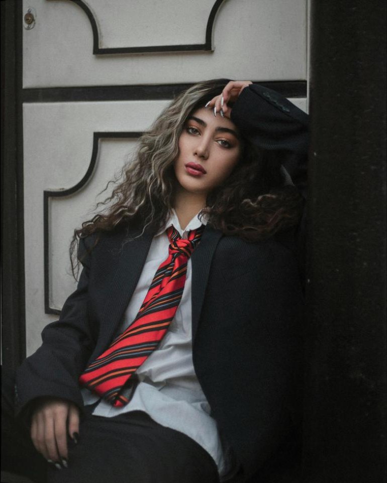 A woman in an oversized dark blazer and white shirt wearing a wide red striped tie