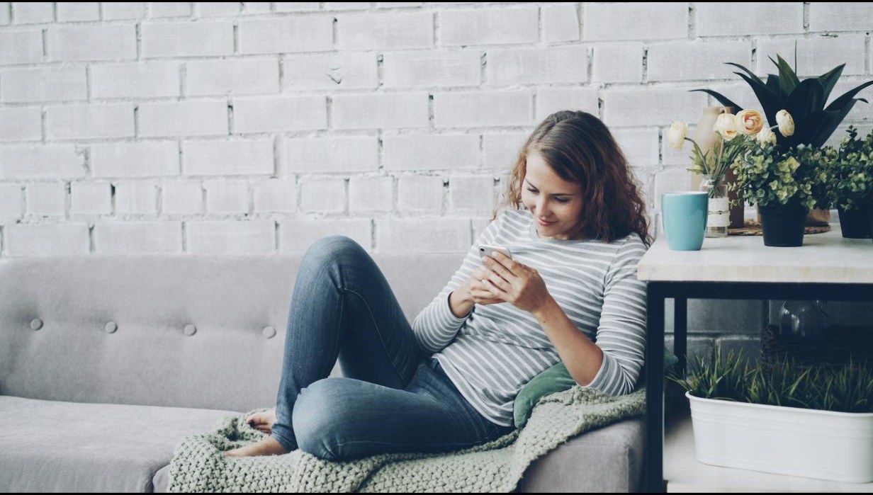 A woman sitting on a sofa scrolling on her phone