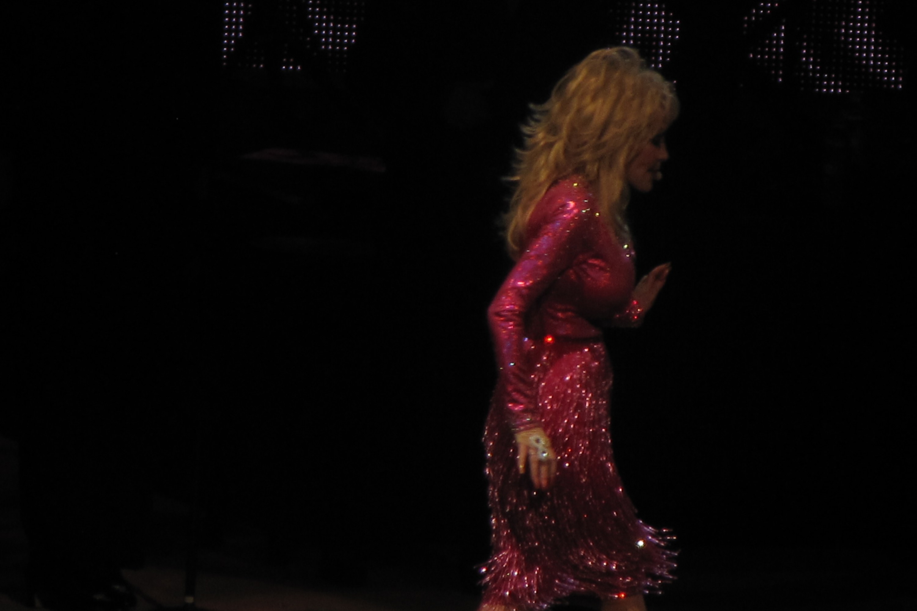 Dolly Parton, in a floor-length fuchsia sequinned dress, crosses a darkened concert stage at Wolf Trap in 2011.
