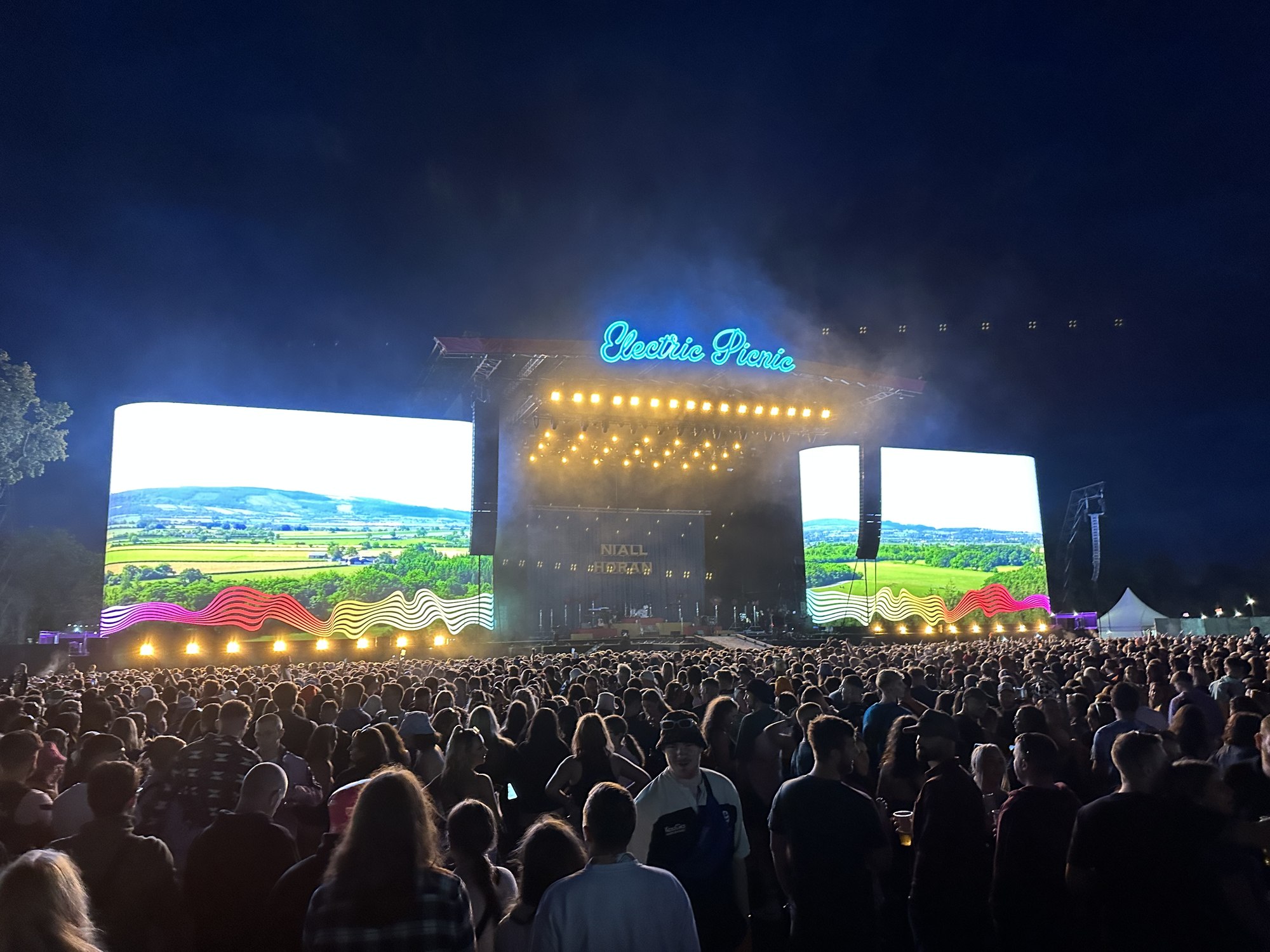 The Electric Picnic main stage lit up at night, its neon sign glowing above a crowd.