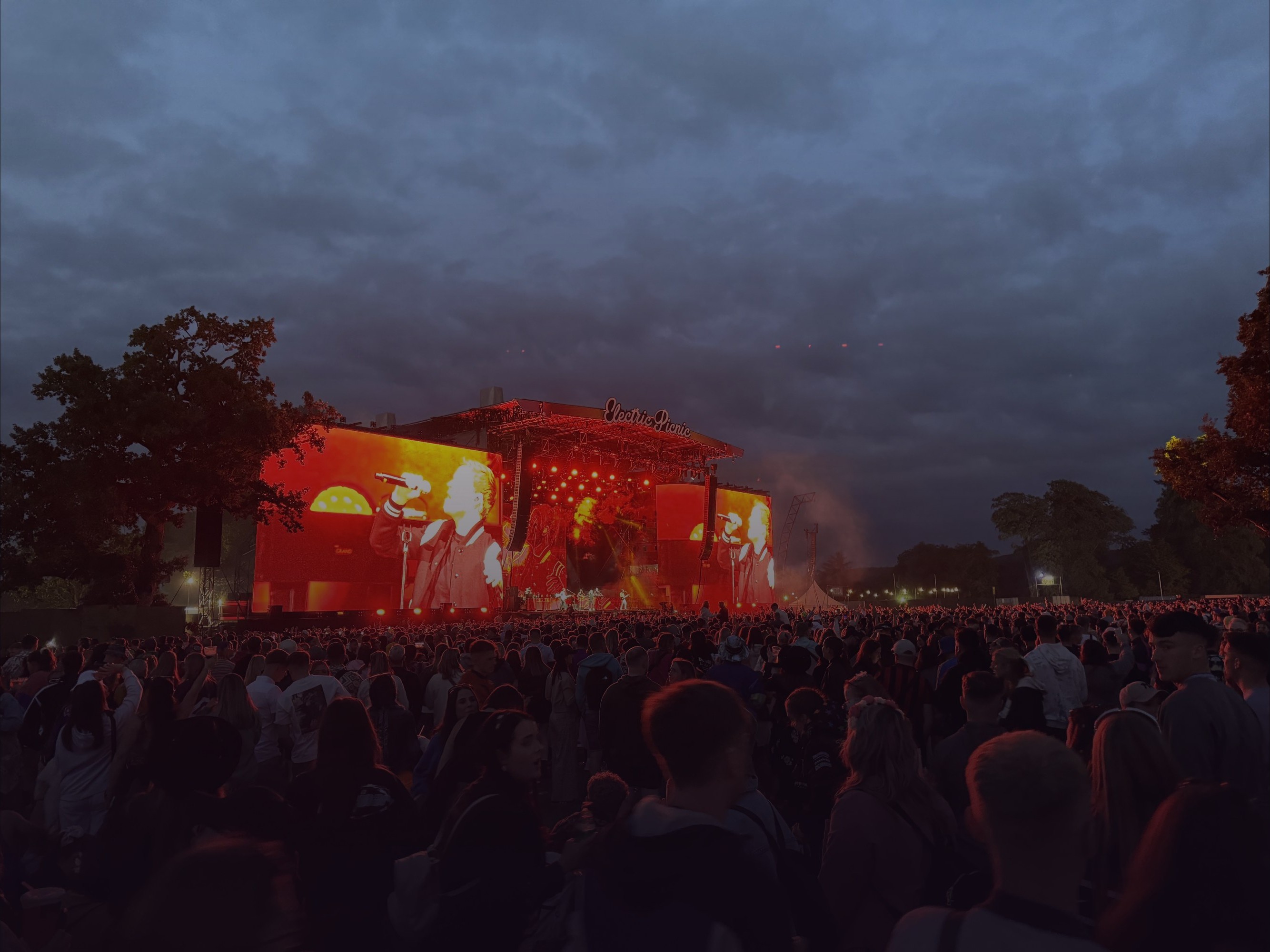 The Electric Picnic main stage lit red at dusk, with a huge crowd in front of it.