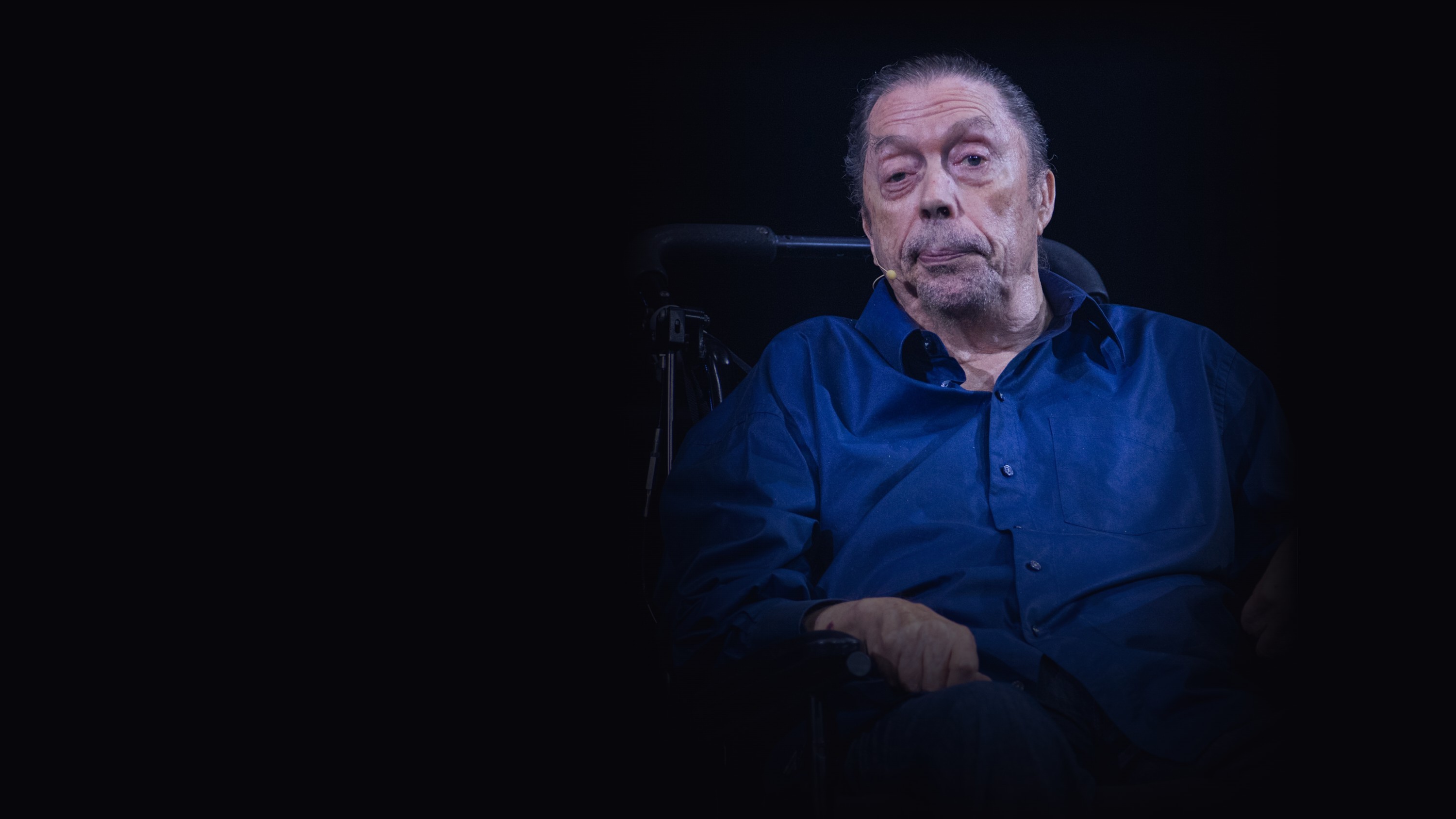Tim Curry, seated, photographed against a black background at a 50th anniversary event for The Rocky Horror Picture Show in 2025.