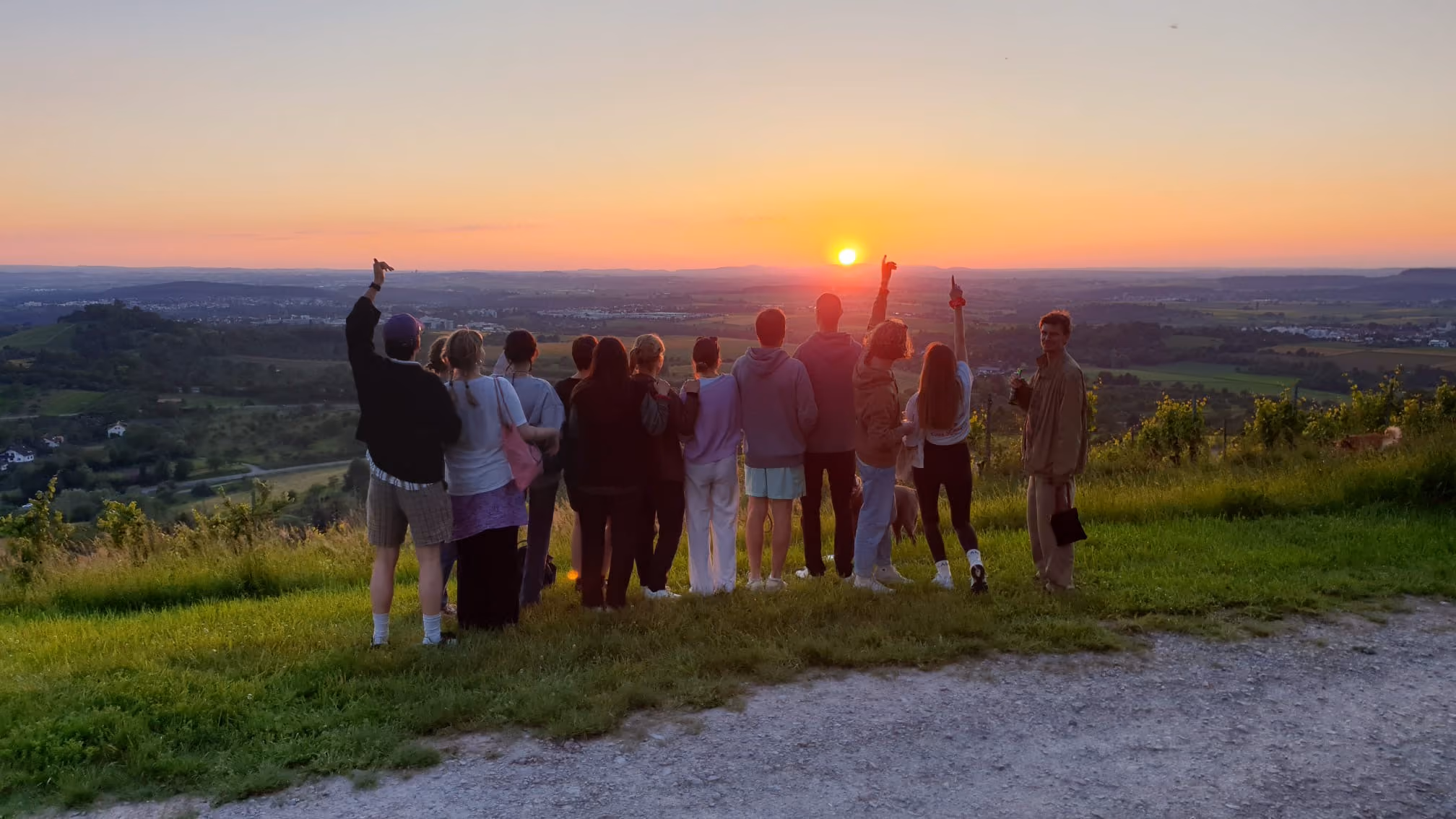 Gruppe steht auf einem Hügel und blickt gemeinsam in den Sonnenuntergang