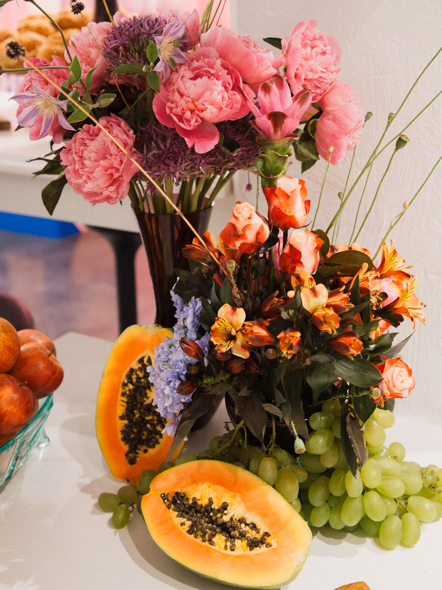 Blumenstrauß mit Pfingstrosen neben aufgeschnittenen Papayas und grünen Trauben