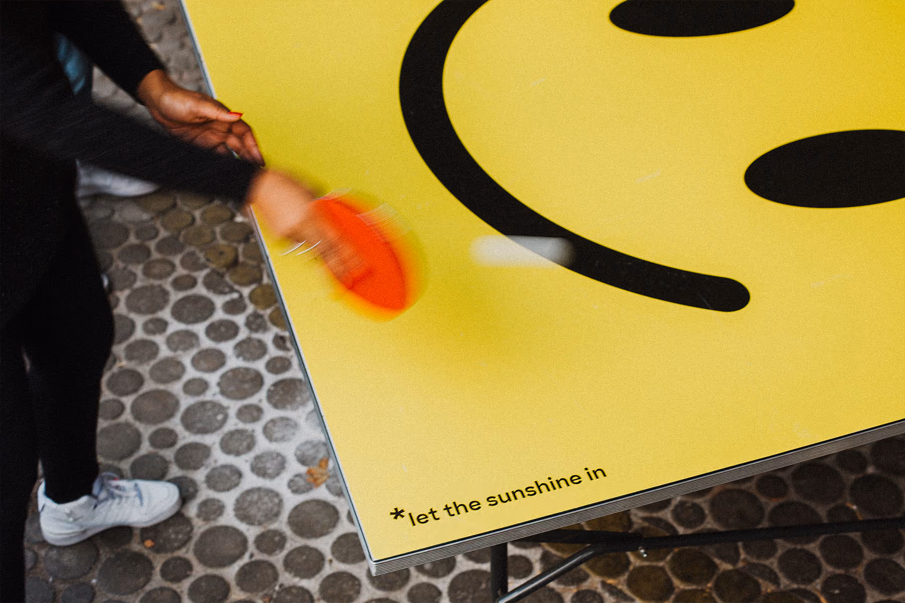 Nahaufnahme eines gelben Smiley-Tischtennistischs mit rotem Schläger in Bewegung