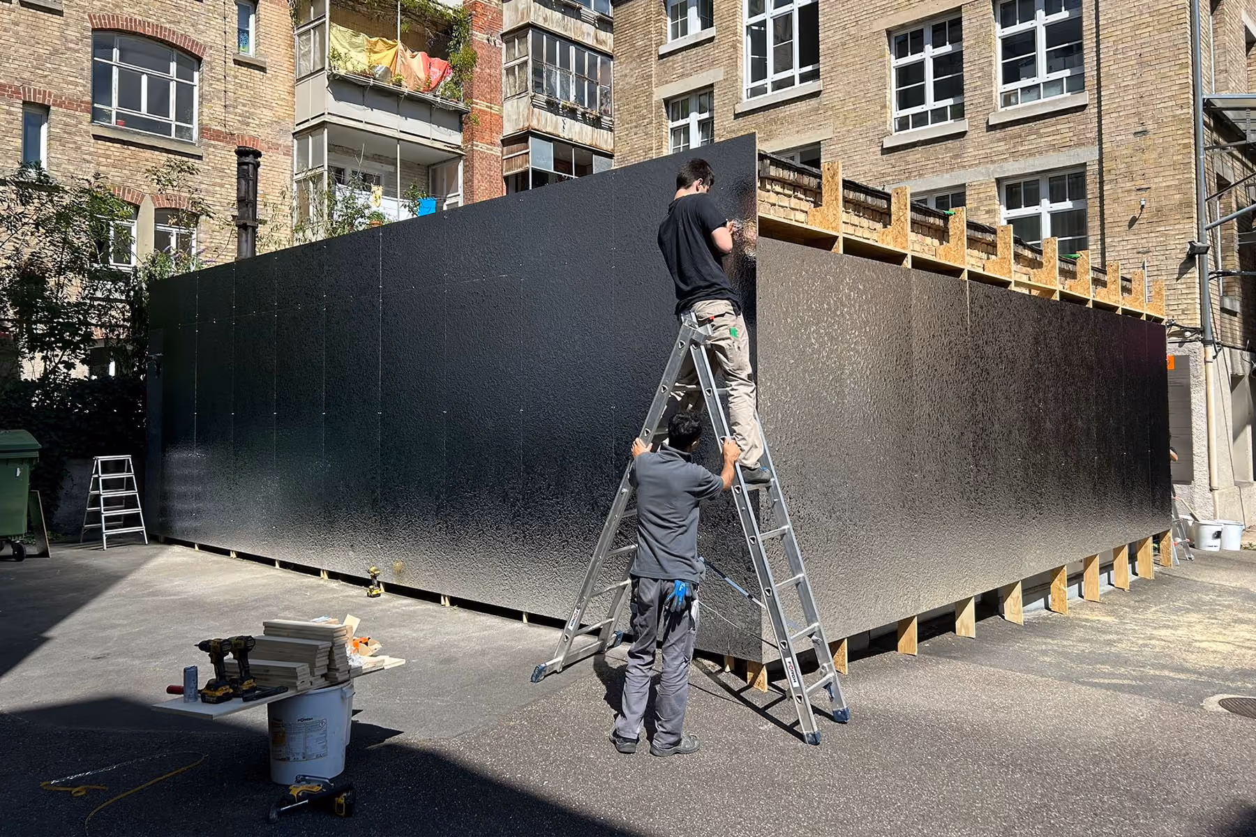 Zwei Handwerker montieren schwarze Wandpaneele an einer großen Standkonstruktion