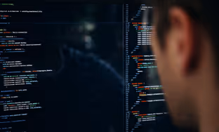 Person looking at a computer screen filled with lines of code in a dark environment.