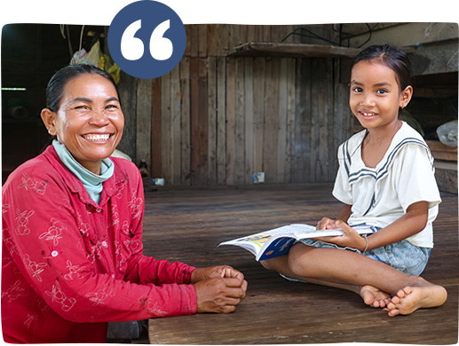 A Cambodian mother sits next to her young daughter as her daughter reads a story book in their home in Cambodia