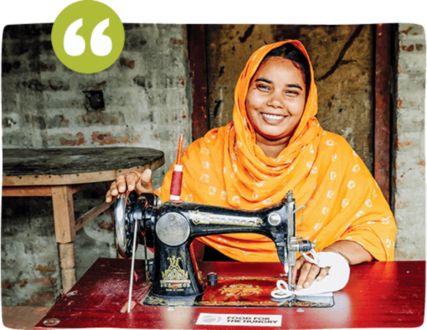 A Bangladeshi woman wearing an orange headscarf sits in front of a sewing machine and smiles while sewing a sanitary pad in Bangladesh