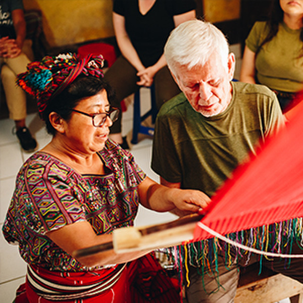 An Indigenous Guatemalan woman explains how to weave traditional Guatemalan fabric to a Canadian man during a vision trip to Guatemala