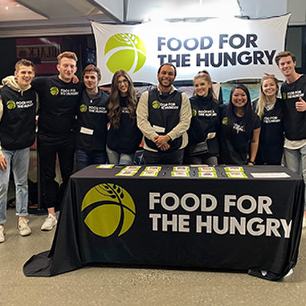 A group of young men and women volunteers stand in front of a booth for Food for the Hungry at an event in Canada