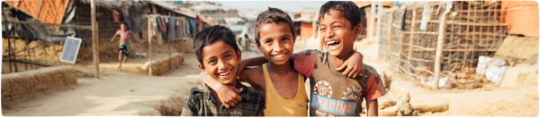 A group of boys from Bangladesh smile with their arms around each other on a village path