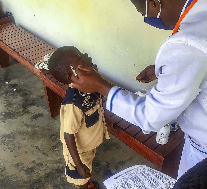 A health worker administers a deworming tablet to a young boy in Uganda