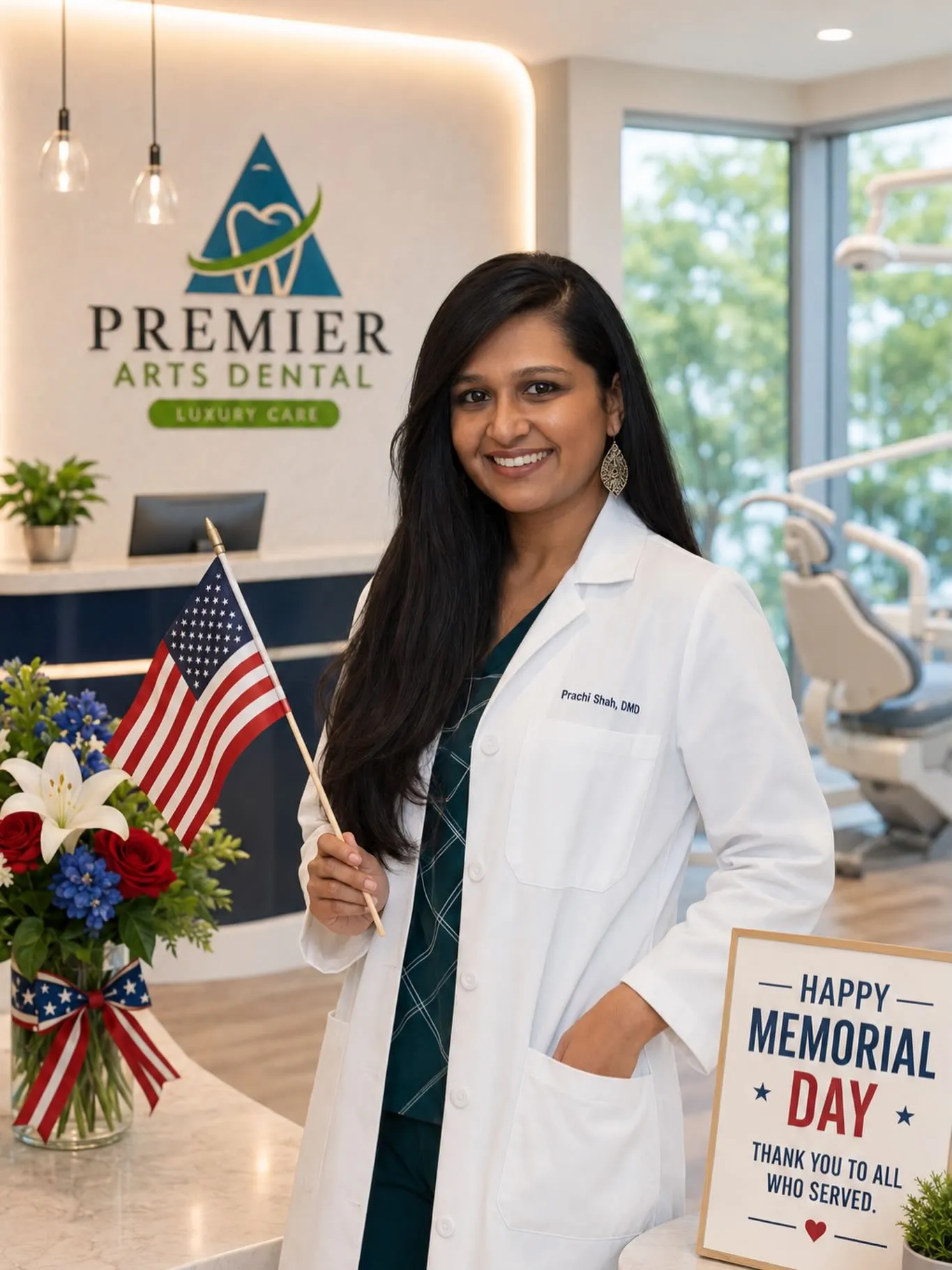 Female dentist in white coat holding an American flag inside Premier Arts Dental with Memorial Day sign.