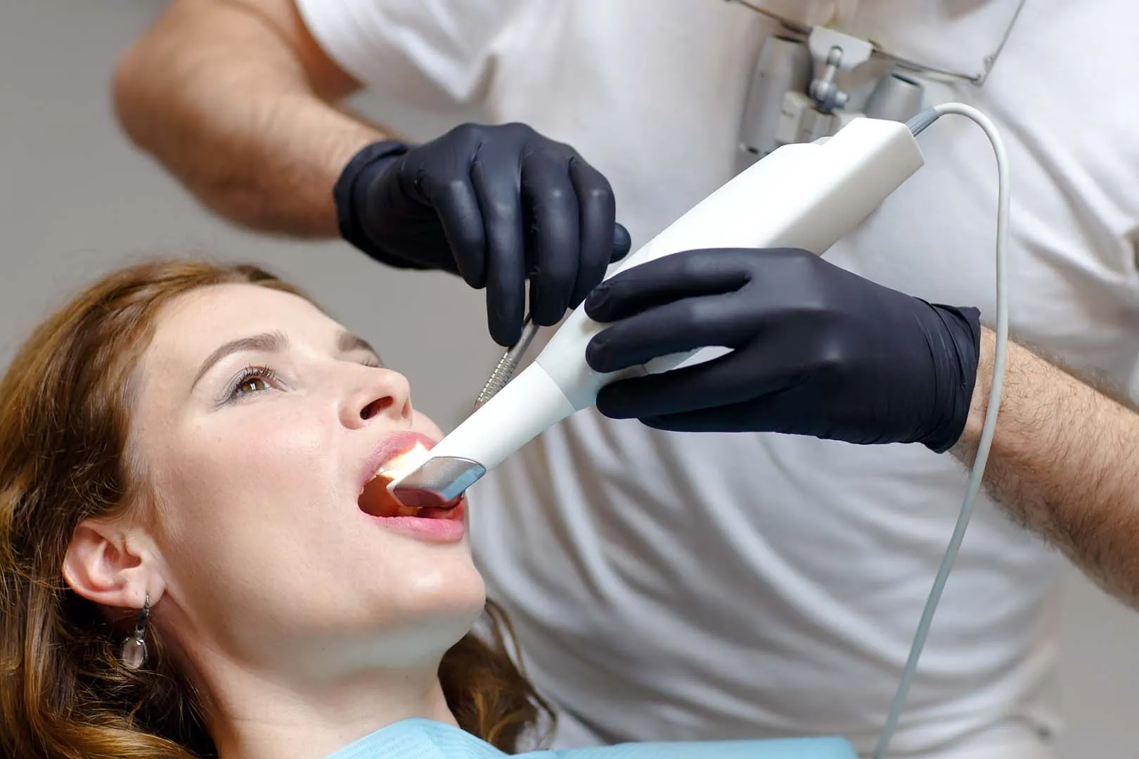 Dentist wearing black gloves uses intraoral scanner for 3D dental imaging on patient.