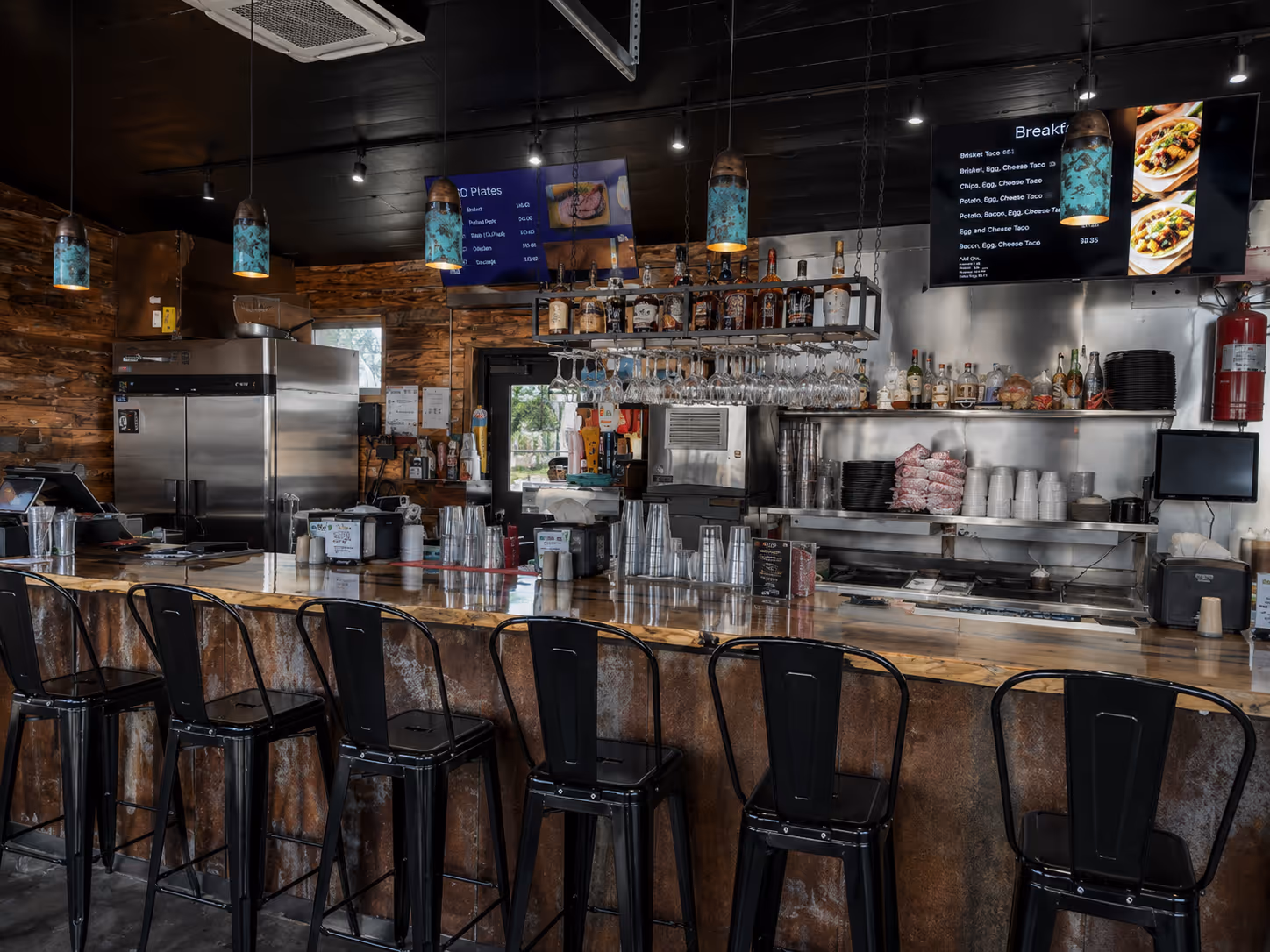 A bar with a counter and stools and a menu on the wall.