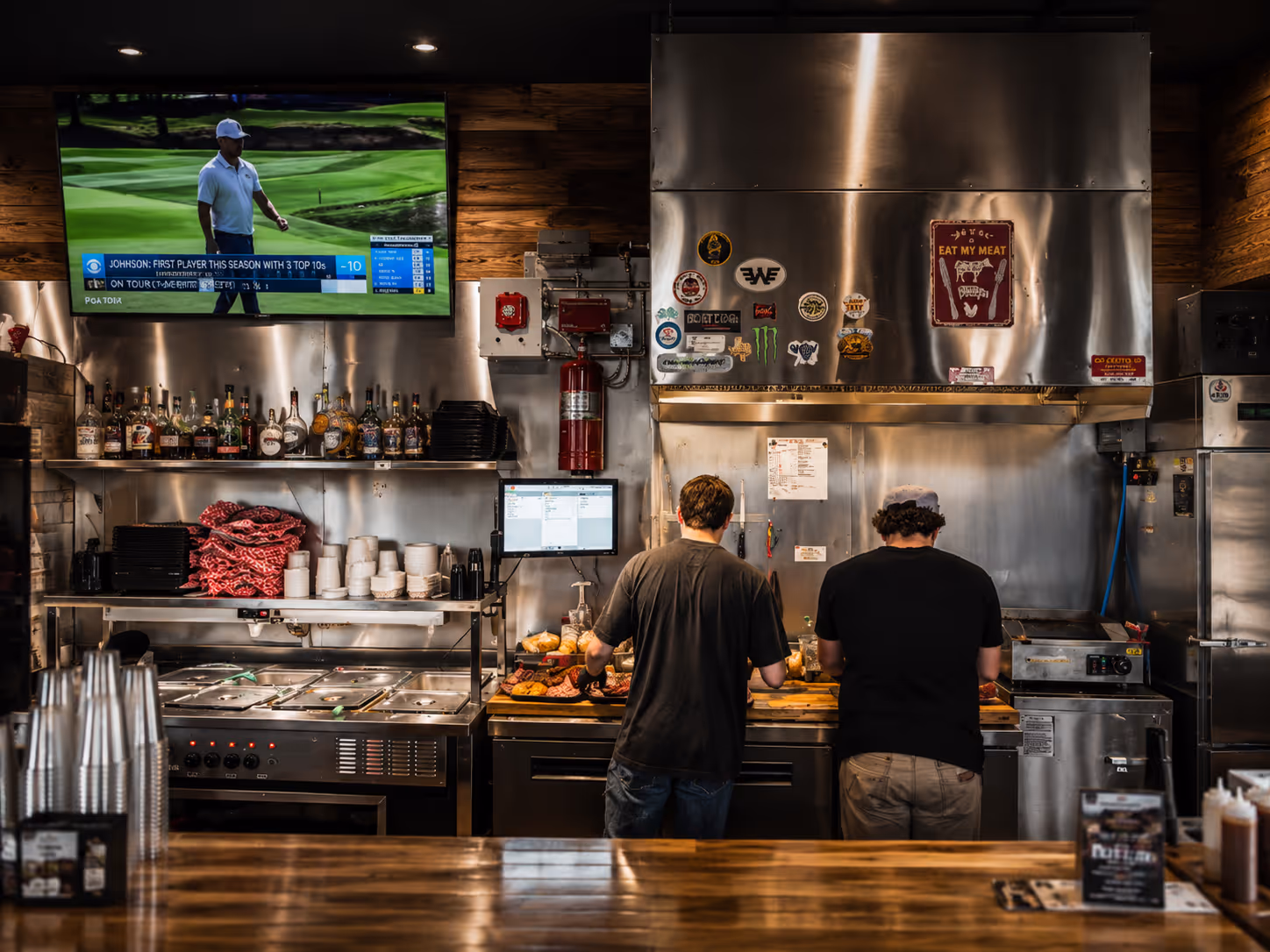 Two men standing in a kitchen in front of a stainless steel counter.