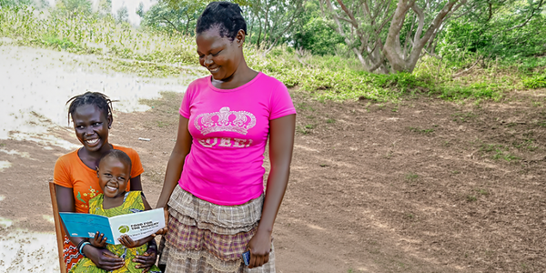 A mother in Uganda reads a book with her two smiling children.