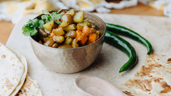 Gajor Alu Vaji served in a hammered metal bowl with green chilies, roti, and a wooden spoon