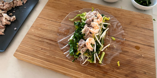 A Kuong spring roll being assembled on softened rice paper with lettuce, noodles, sprouts, pork, and shrimp