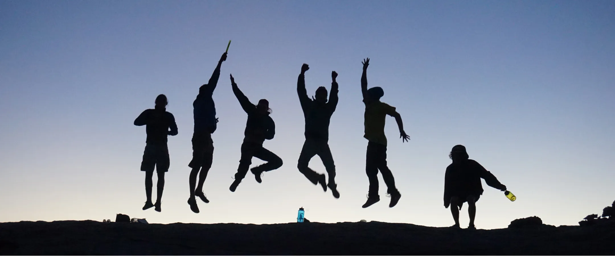 A silhouette of Colorado Rocky Mountain School students jumping in the air on a mountaintop.