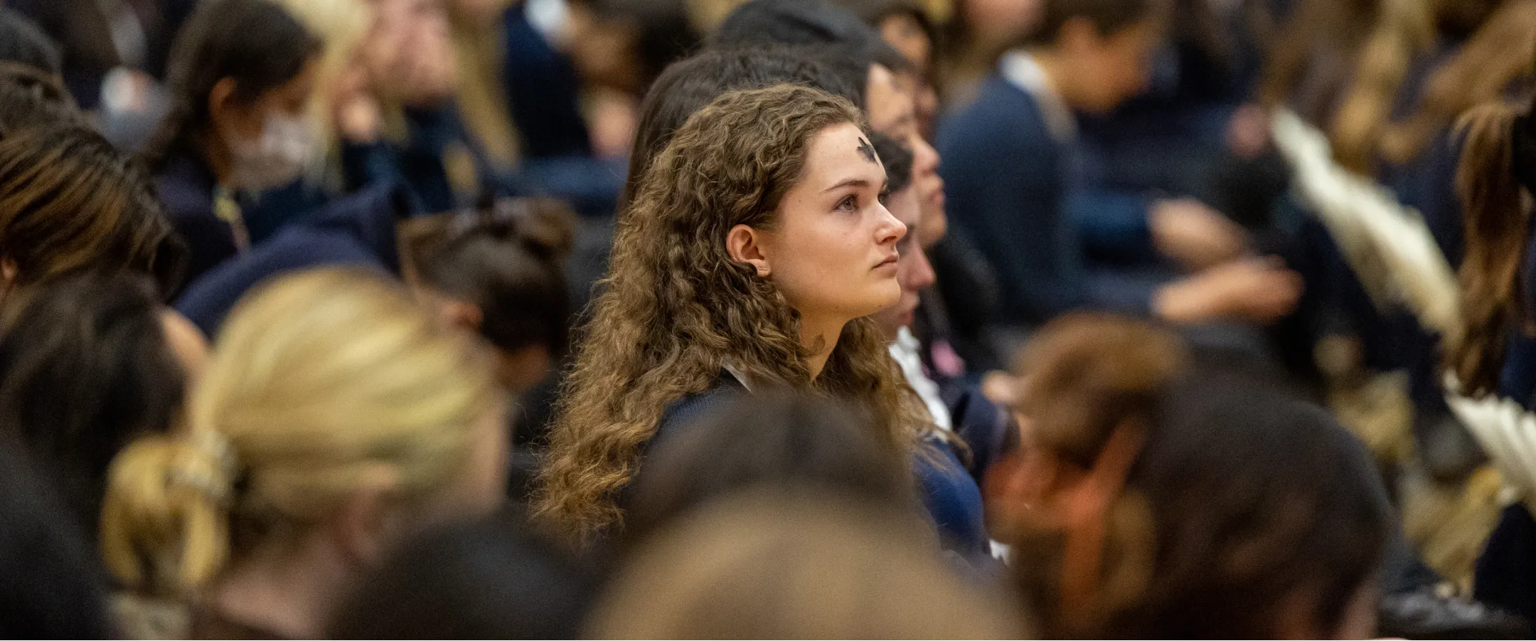 A Marymount High School student looks up from the crowd at a school assembly.