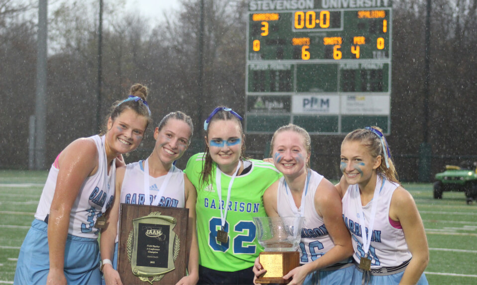 Garrison Forest School field hockey players holding the trophy in the rain after winning the championship.