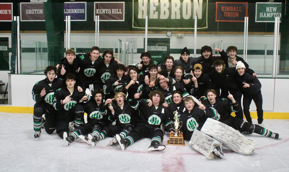 The Hebron Academy ice hockey team posing on the ice with a championship trophy.