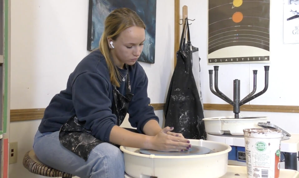 A Hebron Academy student working the clay on a pottery wheel.