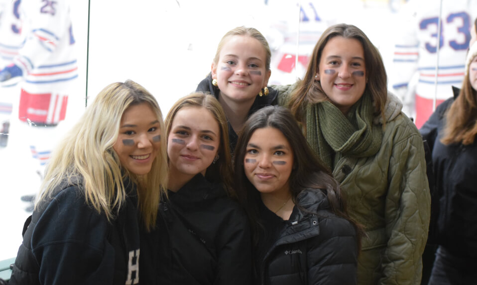 Female students at a Hebron Academy hockey game posing for a picture with eye black on their faces.