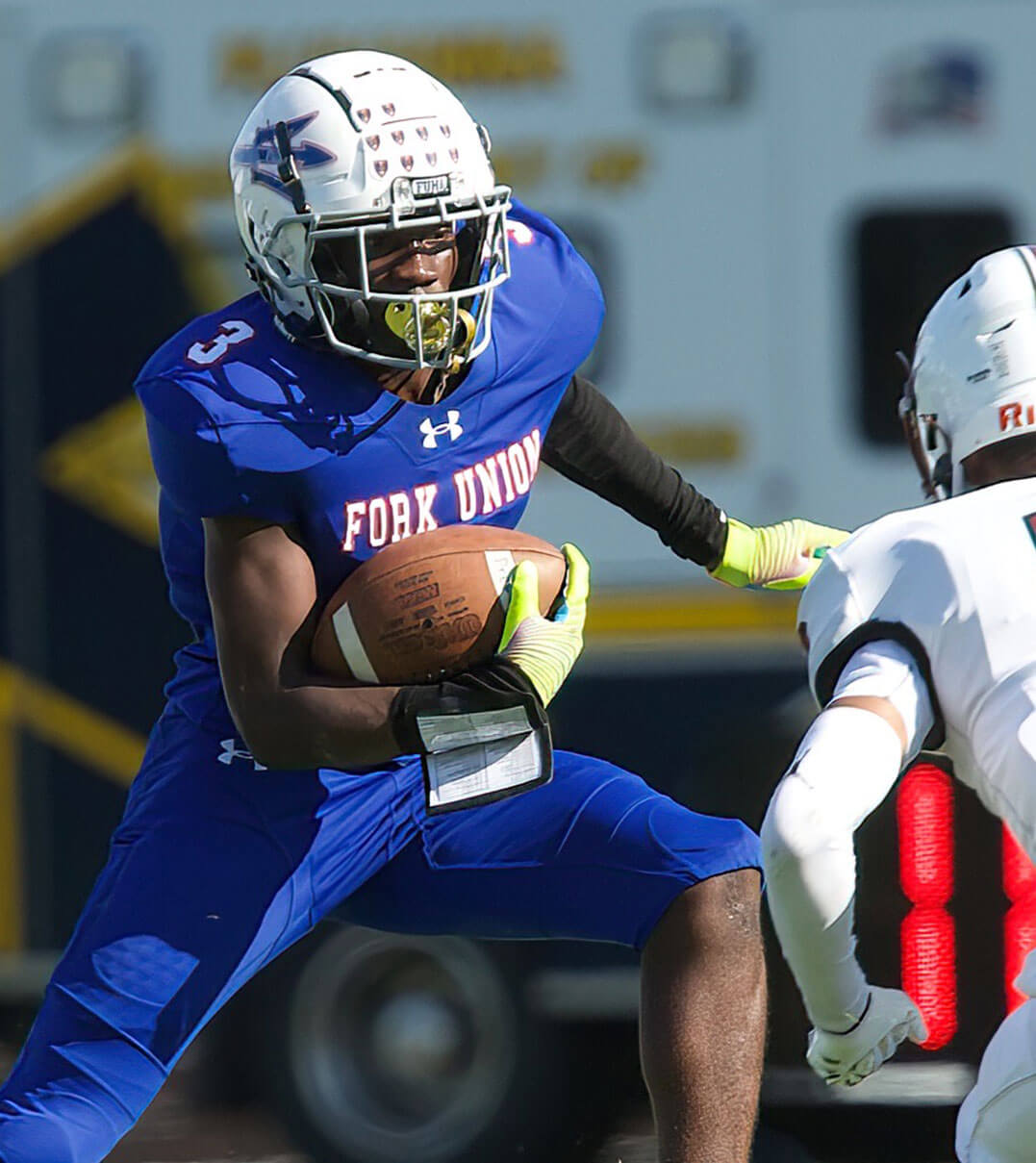A Fork Union football player running with the ball and dodging an opponent.