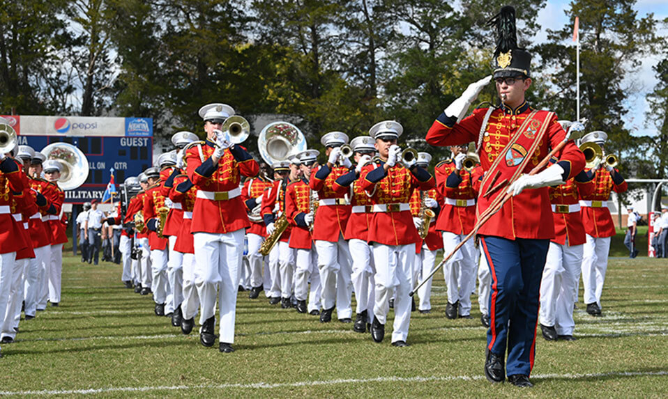 The Fork Union Military Academy marching band in dress uniforms featuring a red coat performing on the football field.
