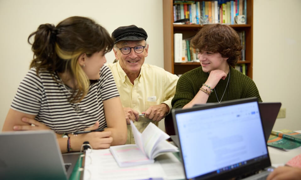 A CSW teacher speaking to two students at a table.