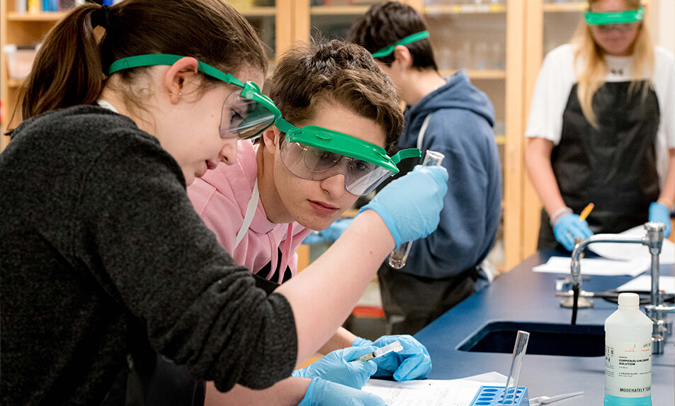 King School students wearing goggles and examining a test tube.