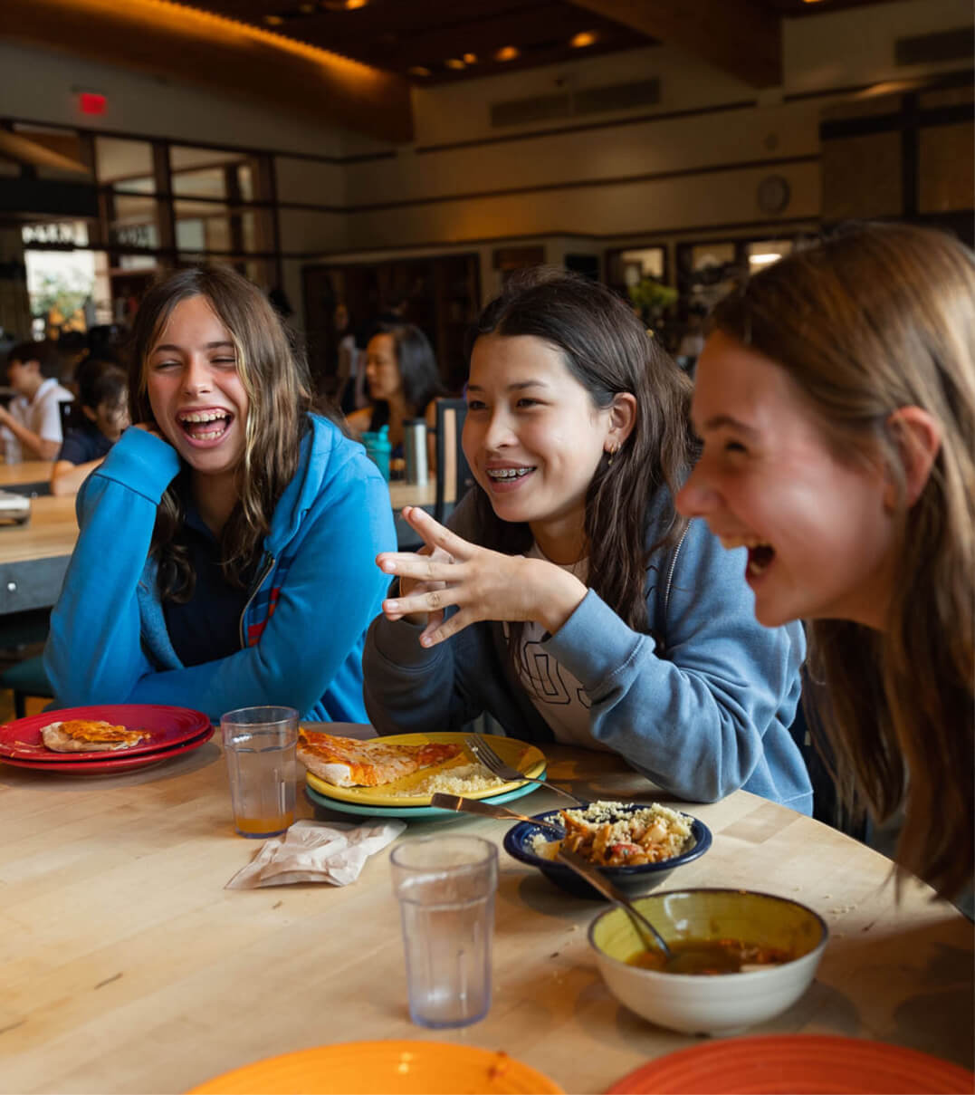 A group of Ross School students talking and laughing at a lunch table.