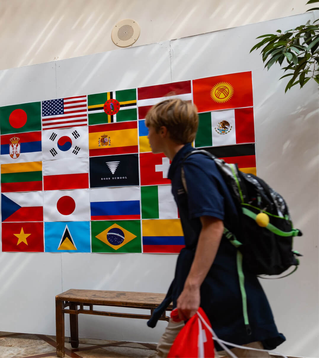 A Ross School student walking next to a board displaying flags from nations around the world.