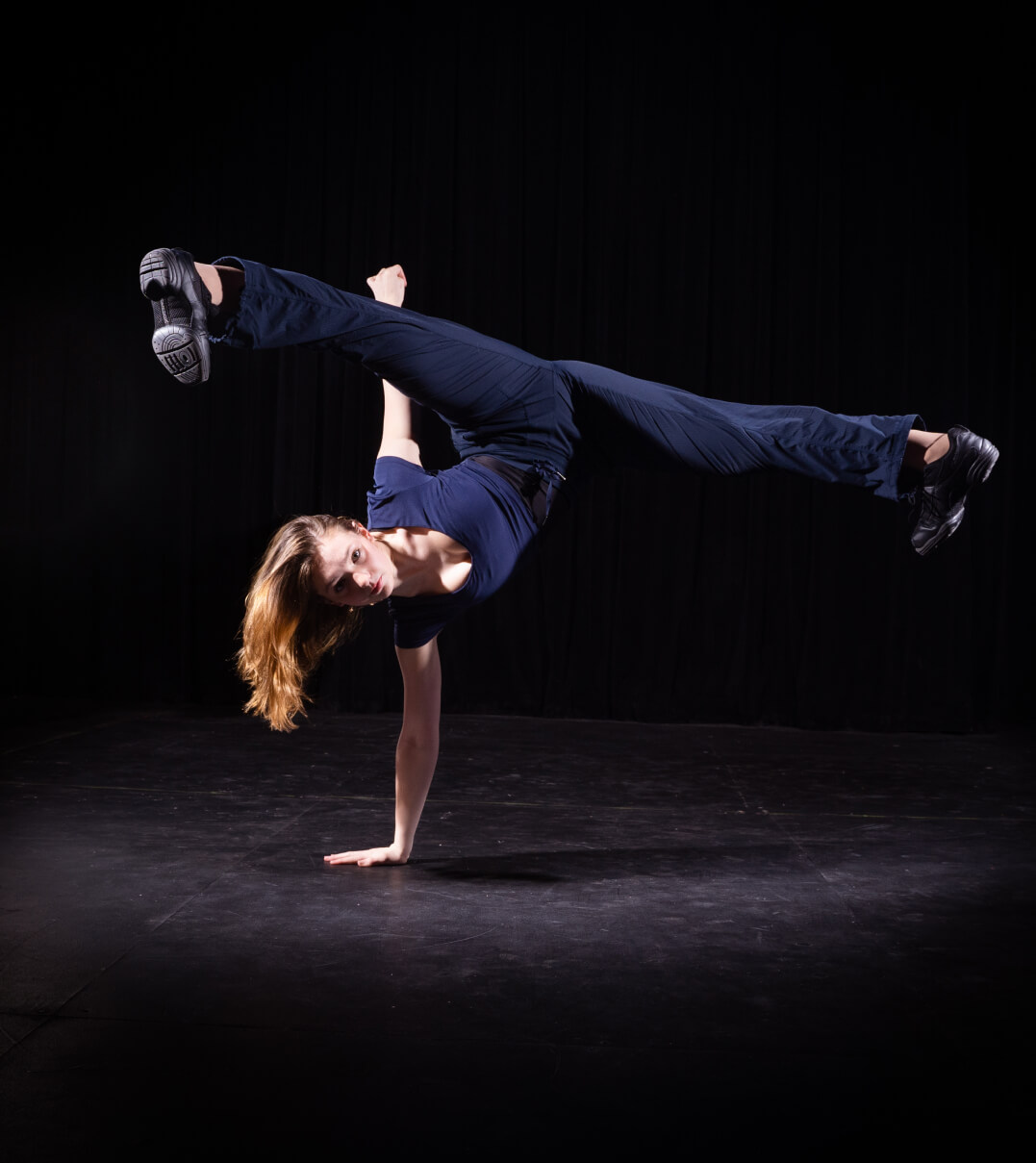 A WMA dancer performs a one-arm break dance move with her legs in a full split in the air.