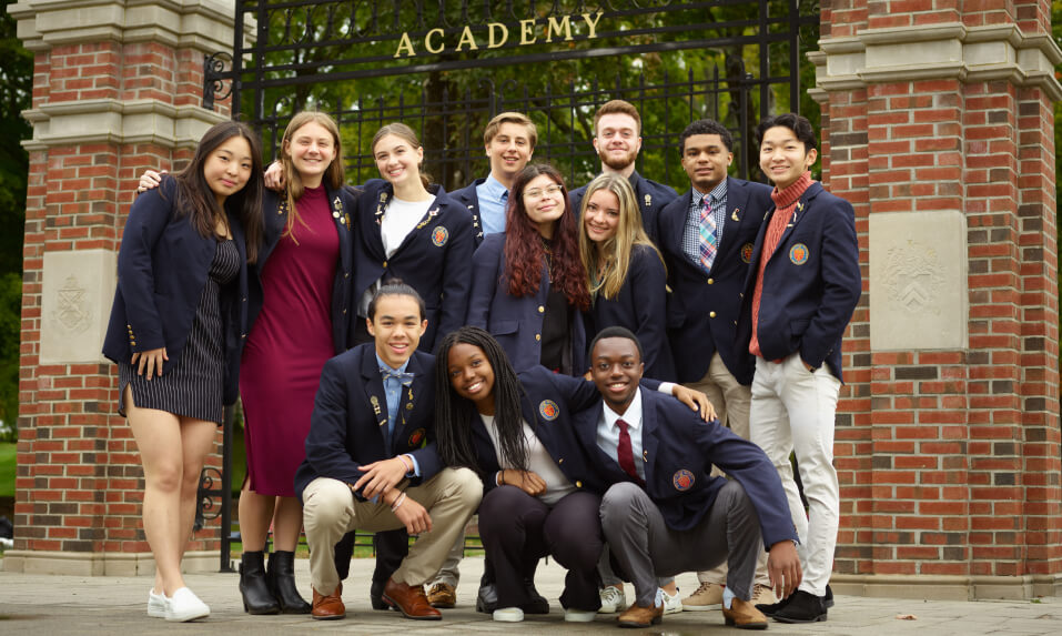 A group of students in their WMA sport coats posing together outside of the school gates.
