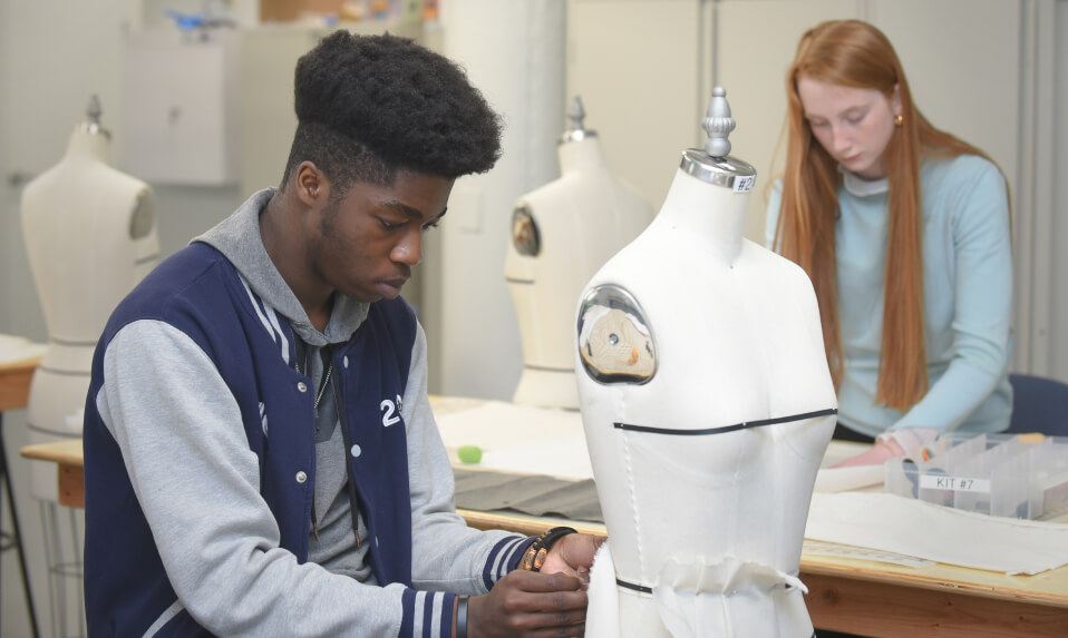 A WMA student affixes fabric to a mannequin in a fashion design course.
