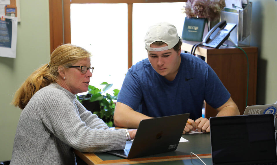 A Proctor teacher pointing something out to a student on her laptop.