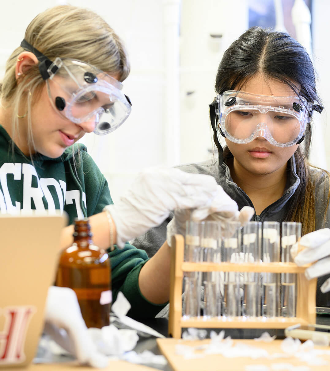 Two Foxcroft School students wearing protective goggles and arranging test tubes as part of an experiment.