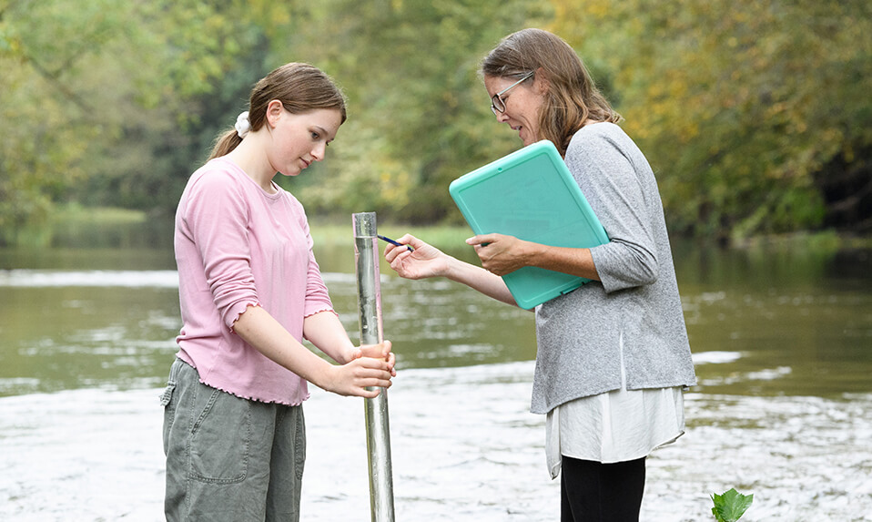 A Foxcroft student and teacher standing in a stream and taking a water sample.